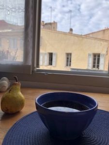 A pear and bowl of tea in front of an open window.