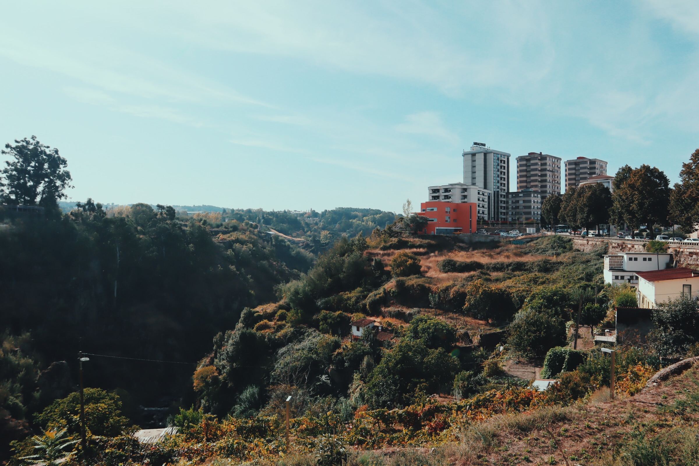 A few small buildings that look similar to a hotel or apartment complexes sit atop a green hill overlooking a valley