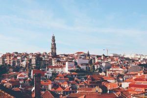 A view of red rooftops of a city. The steeple of a church looms in the distance offset by a blue cloudless sky