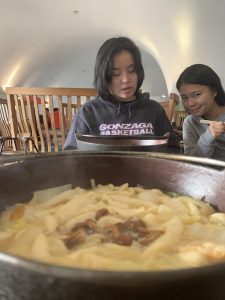 A bowl of food in the foreground, and two girls eating behind it.