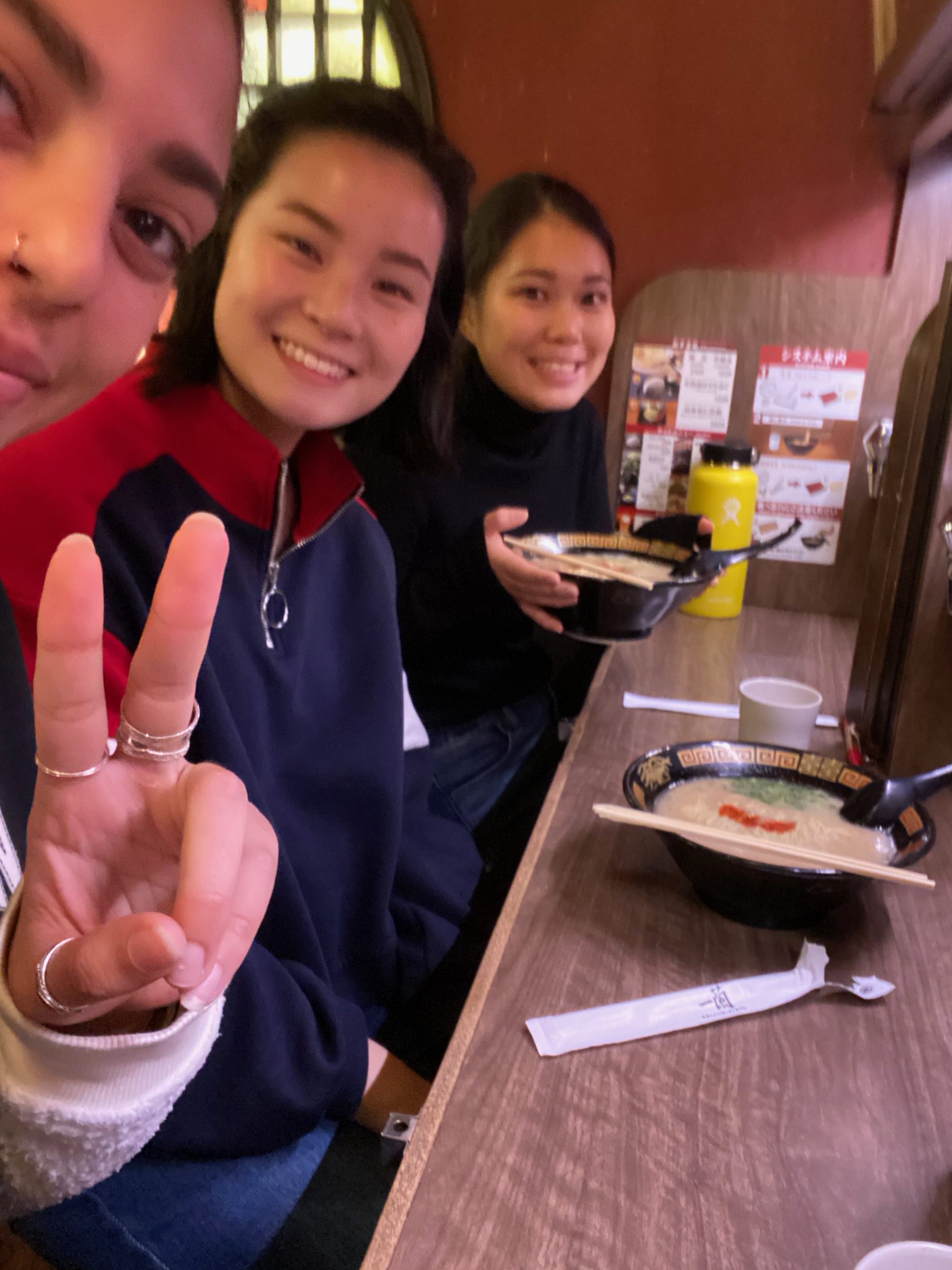 Me, Isis, and Emi at an Ichiran counter with bowls of ramen in front of us.