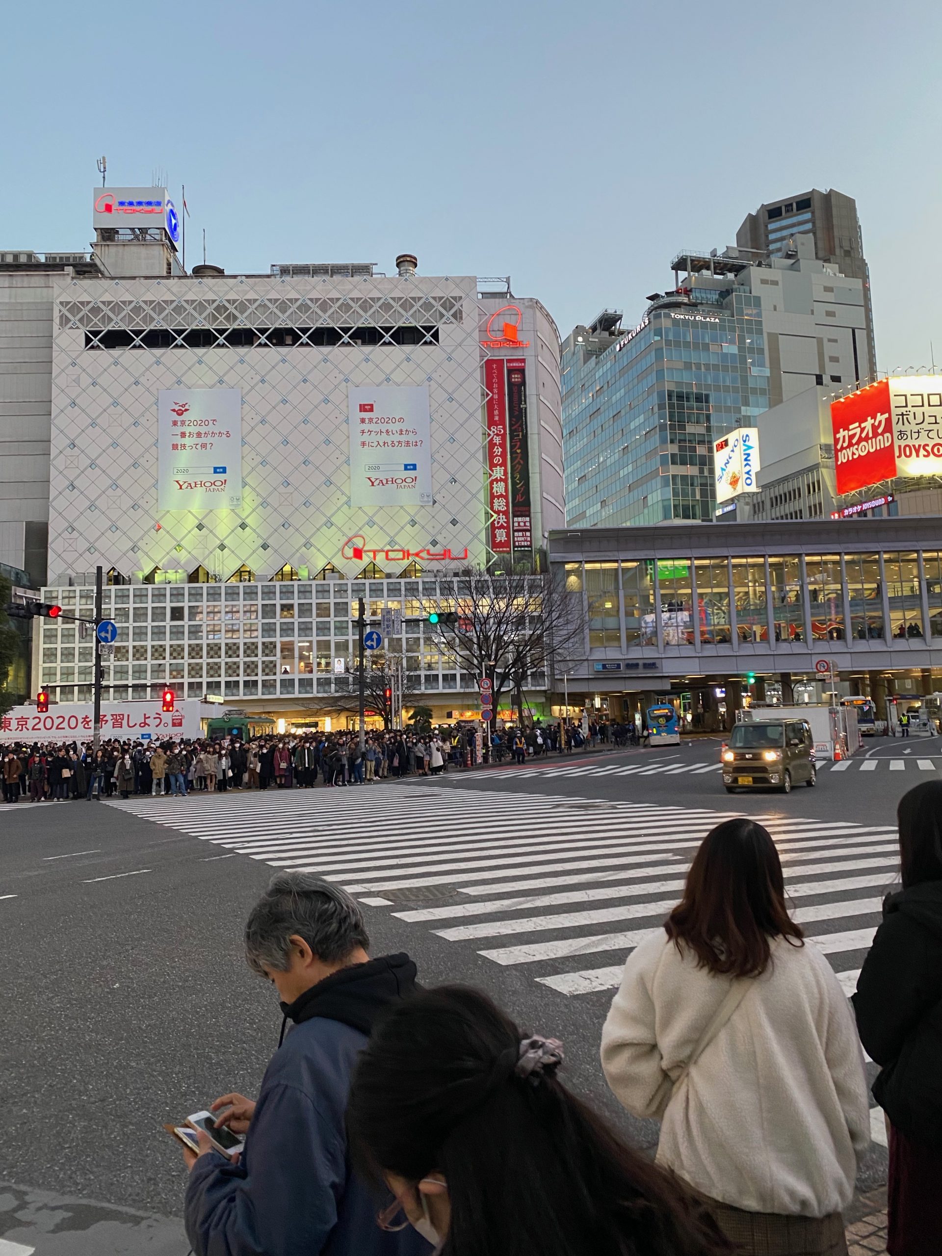 A large crowd of people waiting on the sidewalk to cross at Shibuya Crossing
