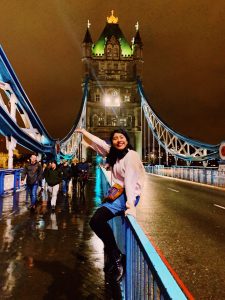 Girl sitting on Tower Bridge at night with bridge lights in the background.