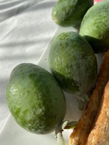 Green fruit on a plate in the sunshine on a white tablecloth.