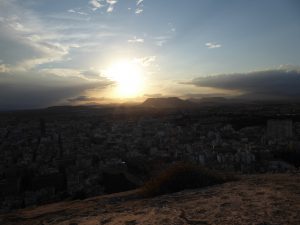 View from atop the castle of Santa Barbara in Alicante, Spain at sunset. Captures  the sun setting amid clouds. 
