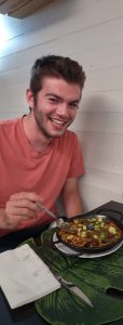 The author, pictured in a pink shirt and smiling, eating a vegetarian paella dish, which includes rice, mushrooms, green veggies, and red fruit. 