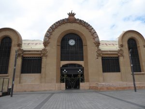 The Central market of Tarragona, as viewed from outside. The windows are tinted black and the walls are brown. Has an arched design.