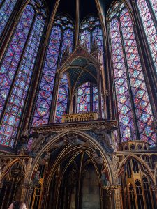 Hundreds of colored glass windows of red, blue, green, yellow and purple in an arched church. In front is an ornate worship box for prayers.