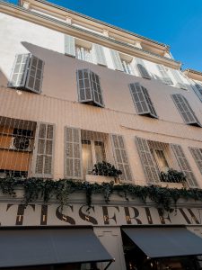 Looking up at the Patisserie with windows to apartments above. The building is decorated with hanging twinkle lights and hanging plants over the side of the patisserie. 
