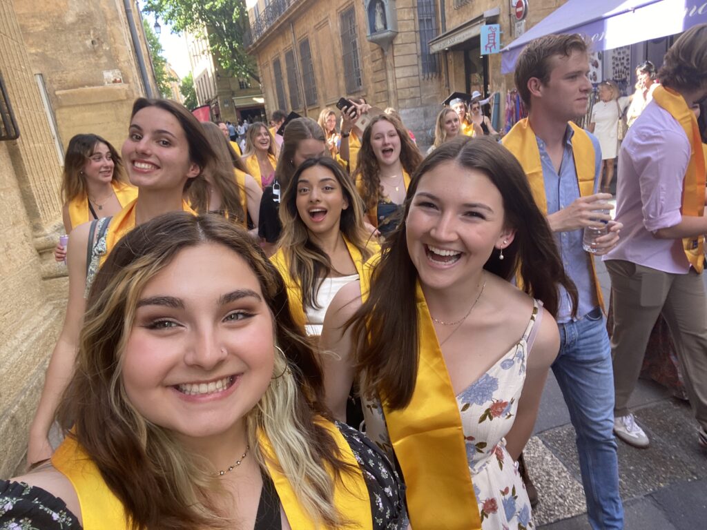 Multiple smiling college students wearing bright yellow stoles walk the street