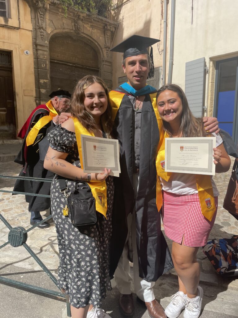 A professor stands in between two female students who are holding certificates