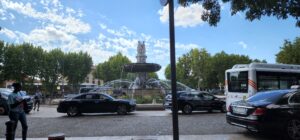Sunny day at the rotonde. In the center of the photo is the large fountain with three women sculpted on top. Surrounded by trees and cars, the Rotonde is a centerpiece of the town