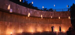 Large wall on the outside of a theatre illuminated by candles on the ground and "floating" lanterns made by candles in tee-shirts. 
