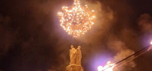 Large, metal chandelier adorned with a myriad of candles hung from a crane over the Rotonde Fountain