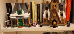The finished Hogsmead Harry Potter Lego Set with two buildings: the sweets shop and the tavern. Alongside the buildings are a myriad of minifigures and there are a collection of french books behind them.