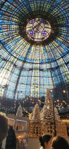 Large stained glass dome at the top of the Printemps (Spring) department store. Sunlight cascades down onto the winter sportswear shop underneath it, which is decorated by snow flocked fake trees and string lights.
