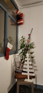 A plush Santa hangs from a pole in the corner, a stocking hangs from the window hatch on the left hand side, and a small wooden tree sits on a dark brown table, each branch consisting of direction signs pointing towards different holiday activities and treats