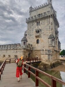 Girl in red outfit walking towards Belem tower on a cloudy Lisbon day