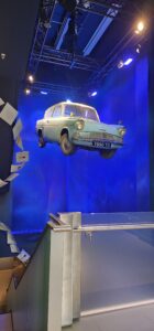 A light blue car floats levitated off the ground below it with a blue background surrounding it on two sides. Traces of Hogwarts letters that lead one downstairs can be seen on the left side
