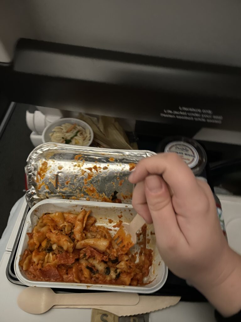 pasta with tomato sauce in a foil container. A hand holding a wooden spork above the pasta