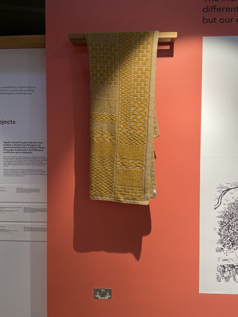 A mustard yellow woven cloth hanging on a salmon pink wall