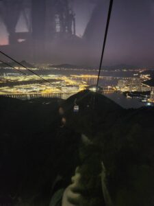 View over the hills, water, and the lights of Hong Kong at dusk, on the last stretch of the cable car ride. 