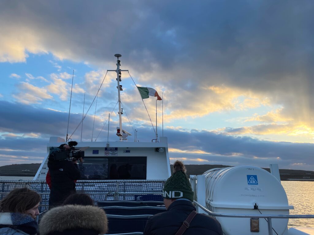 the top deck of a ferry during sunset. The ferry is flying the flag of Ireland