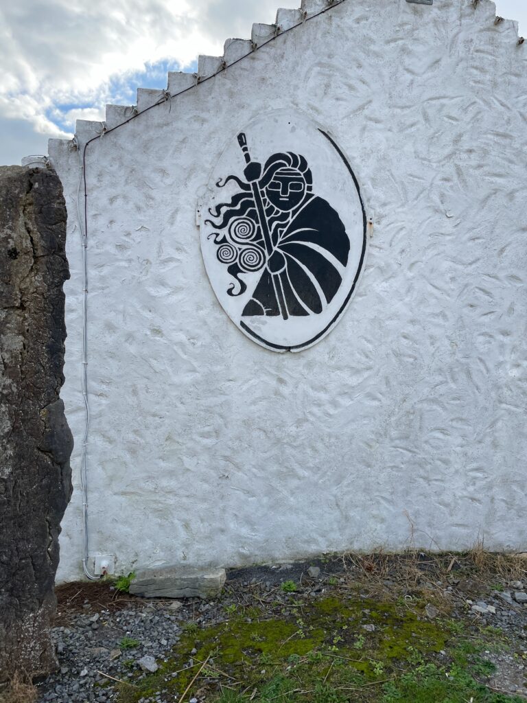 traditional celtic style art of a woman holding a stick, positioned on the side of a white-walled building