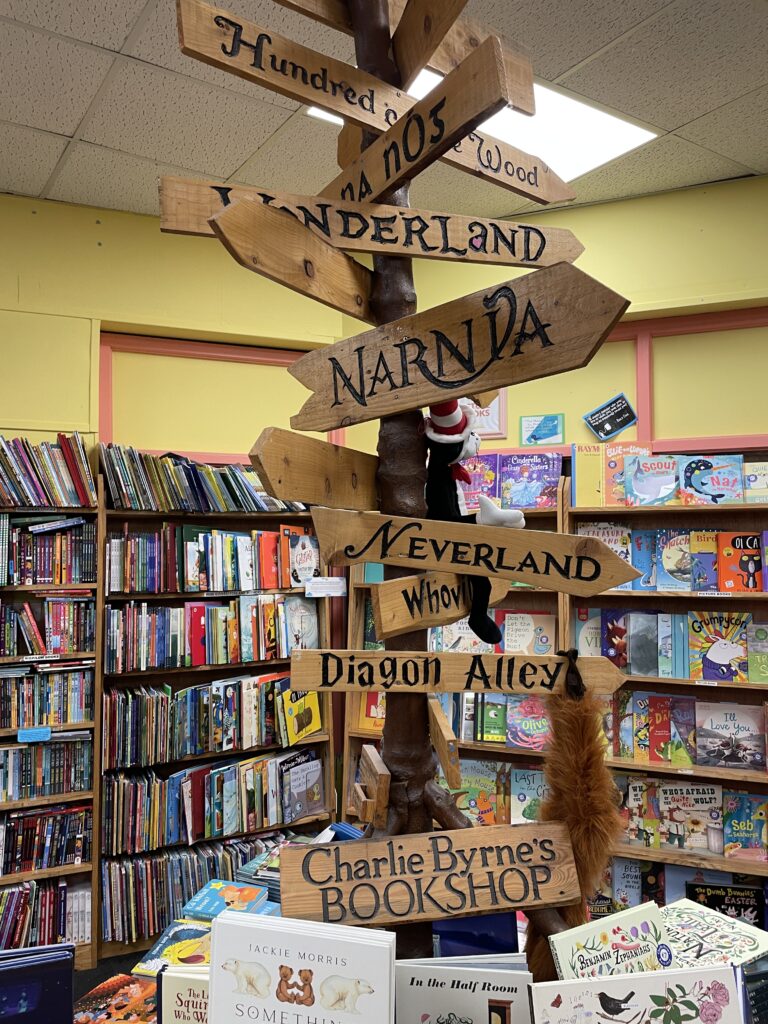a wooden sign with arrows pointing to different places as depicted in works of literary fiction, including wonderland, narnia, neverland, and diagon alley