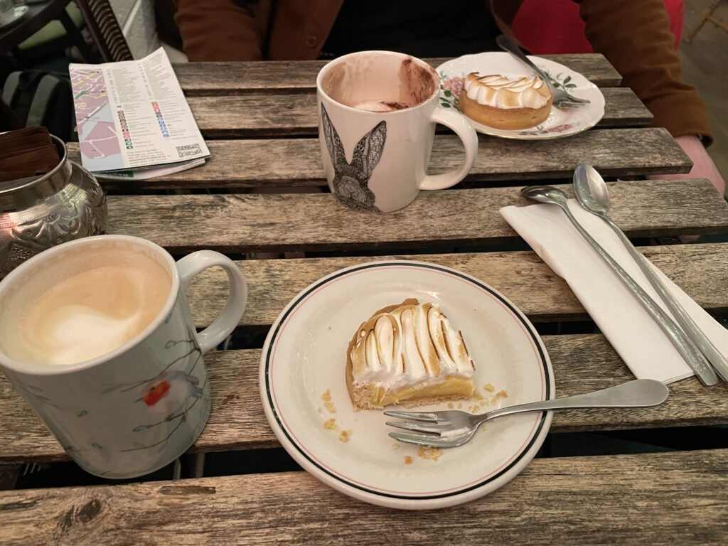 a cafe table with two mugs full of coffee and two plates, each with a lemon meringue tart