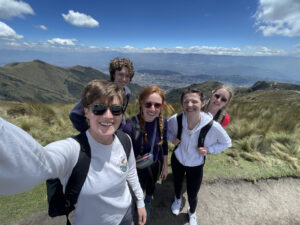 Pictured is my friends and I after hiking the Pichincha trail. In the photo, we are all smiling with the trail, mountains, and sky in the background