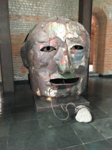 This is an artwork found in a contemporary art museum. It is of a giant face that is made of other smaller faces. The material used for this artwork is metal 