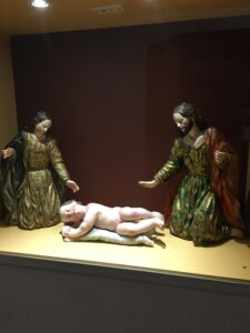 Pictures are glass figurines of Mary, Joseph, and Jesus. Jesus is laying on the ground while Mary and Joseph are in awe of him. 