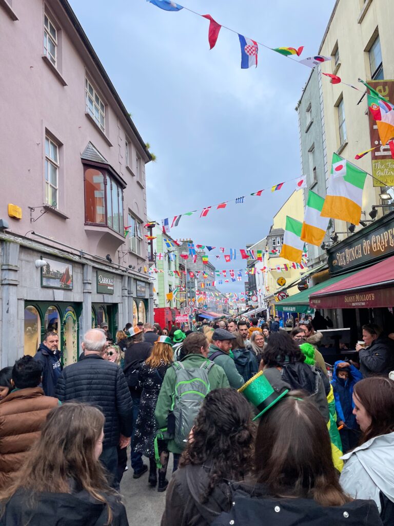 a busy street with crowds of people and Irish flags hanging from a building