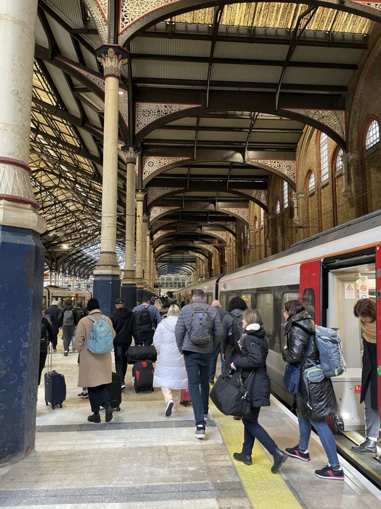 a train station with people on the platform. The ceiling has arches and columns