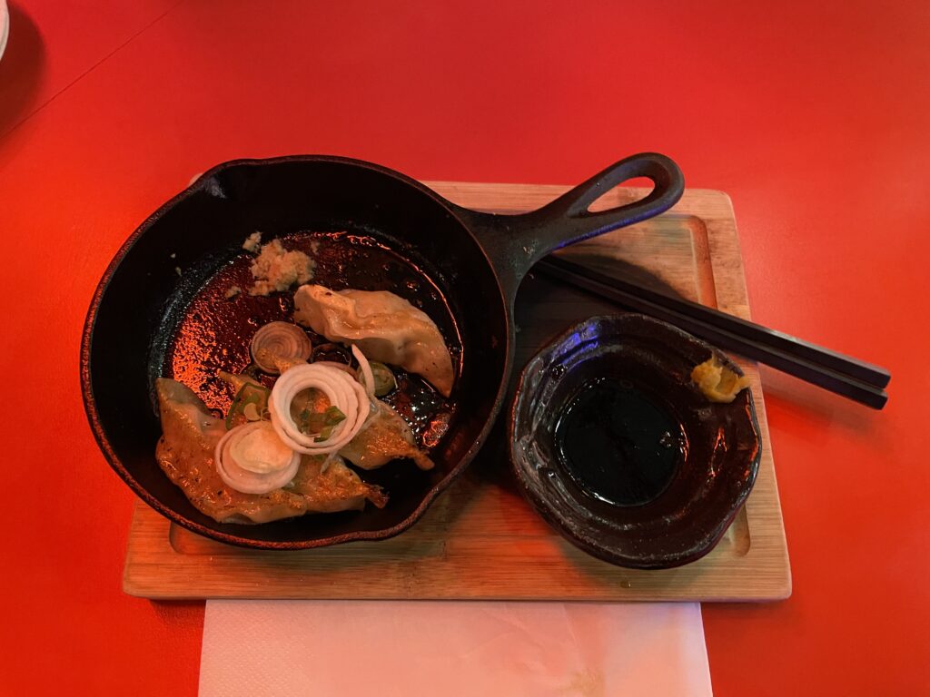 a small skillet with pork dumplings, chopsticks, and a small cup of soy sauce