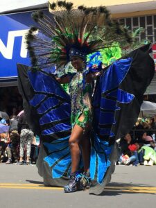 Pictured is a women walking the parade route in Ambato. In the photo, she is wearing a costume with many blue and green feathers. She looks very happy and proud.