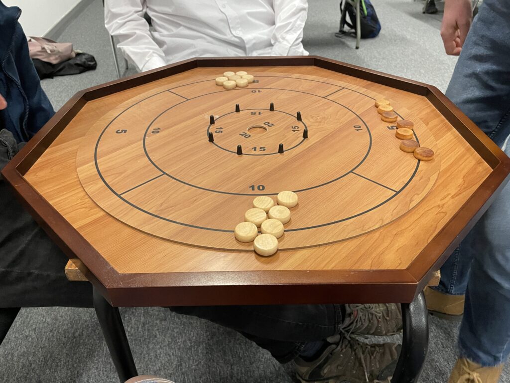 the board game crokinole. a wooden octagon with circles inscribed in it and light and dark colored circular wooden game pieces resting on the board
