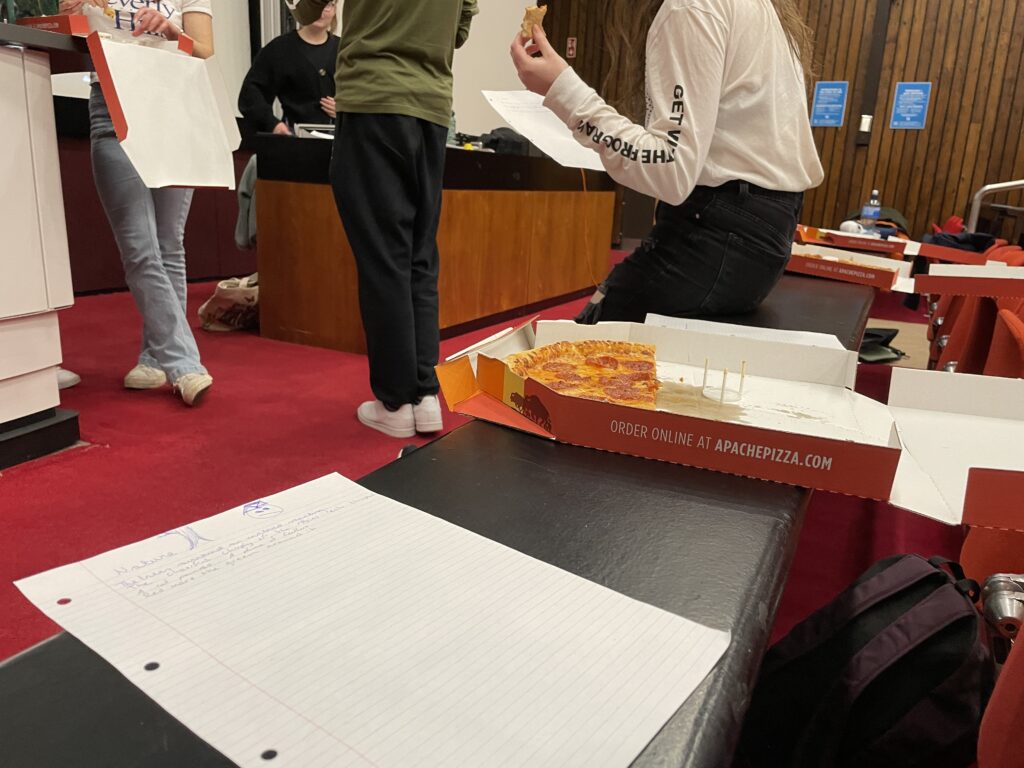a picture of a pizza box and a piece of paper, with students standing in the background