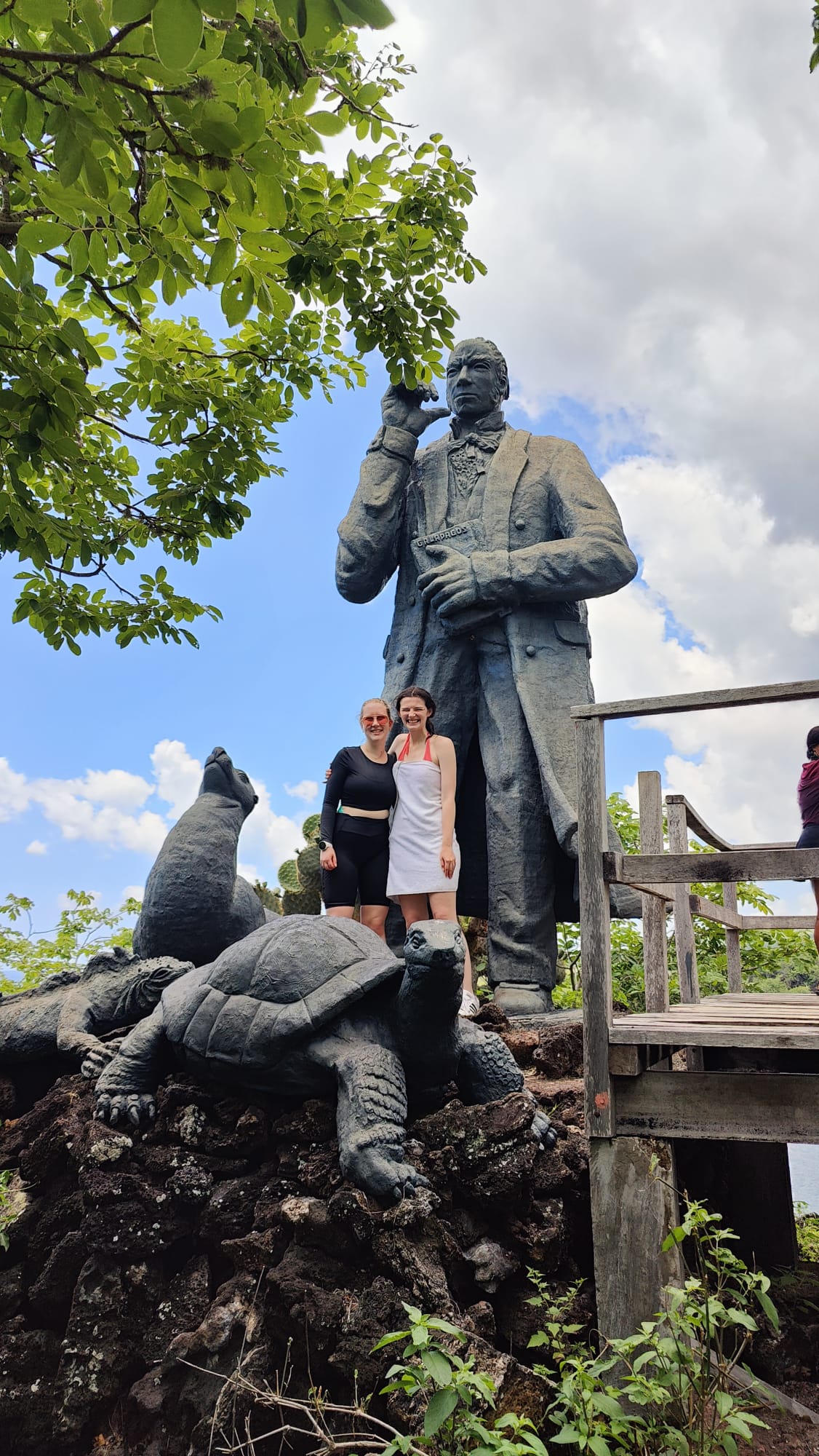 Pictured is my friend Leena and I posing with three statues: one of Charles Darwin, one of a sea lion, and one of a tortoise. We are both smiling with a nice blue sky above us.