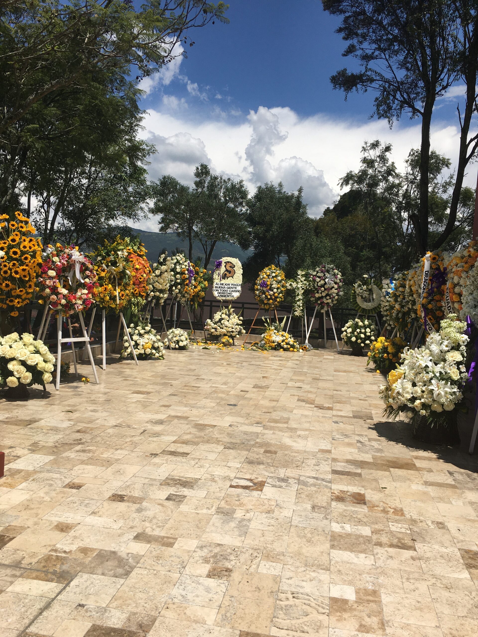Pictured is a memorial for Santiago. In the picture, there are many flower wreaths and crosses propped together to create a closed-off section for viewing. 