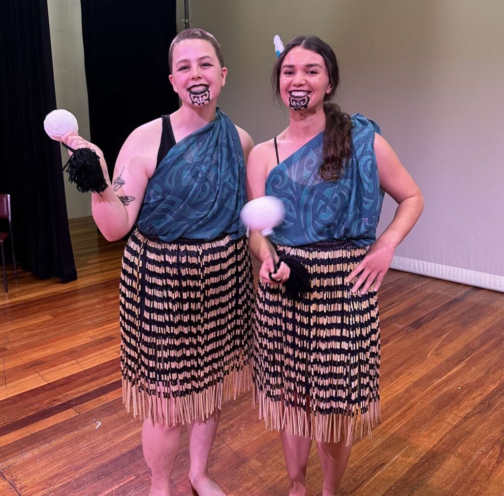 Kahiau and her friend holding their poi, dressed in Maori traditional clothing.