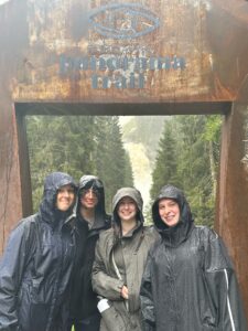From left to right; Sage, Andrew, Rachel, and Lizzie smile in the pouring rain in front of a beautiful waterfall on a hike.