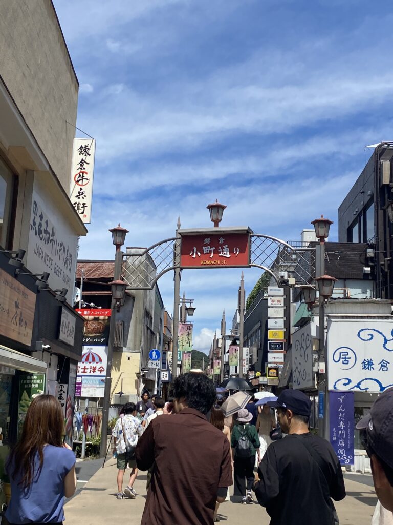 In the center reads a red sign that says "Komachi St." Along the sides there are many signs for different businesses. There are people walking down the street.