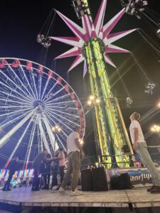 Ferris wheel on the left and in the background, Swing (looks like a tower with pointed petals sticking straight out from the top of it), lighted, on the right and in the foreground