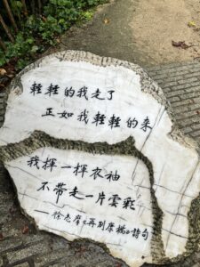 A poem written in traditional chinese characters inscribed on a light colored stone sitting in an alcove next to a patch of grass