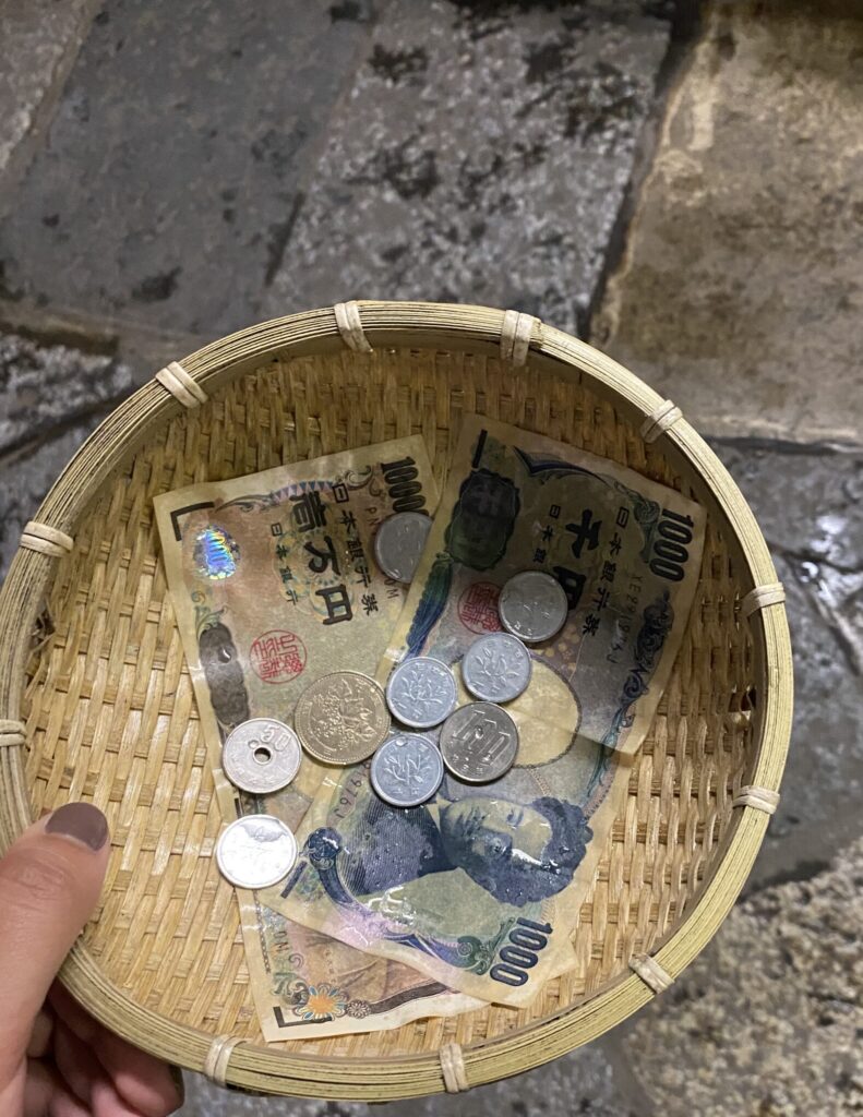 A small woven basket with a 10,000 and 1,000 yen bill, as well as some coins that have been washed in spring water