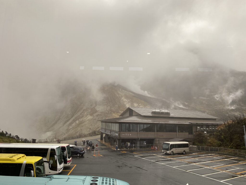 A view of Owakudani Sulphur Mountain. There are clouds of sulphur passing that look like very dense fog. The geology museum can be seen towards the bottom right corner. 