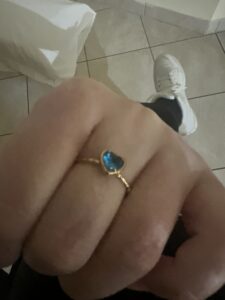 Fist showing a gold ring with a blue heart stone on the middle finger