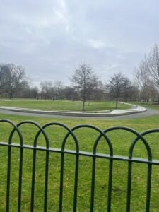 A far away shot of the Princess Diana fountain. A curved long stretch of flowing water enclosing and surrounded by a large field